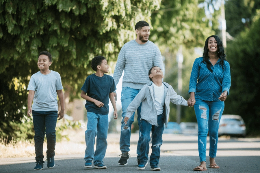 Happy family of parents and three kids walking through neighborhood 